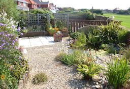 Pebble filled walkways with inset sleeper path, colour filled flower borders, pond and seating area